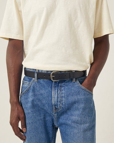 Person wearing a beige shirt and blue jeans with a black belt on a plain background
